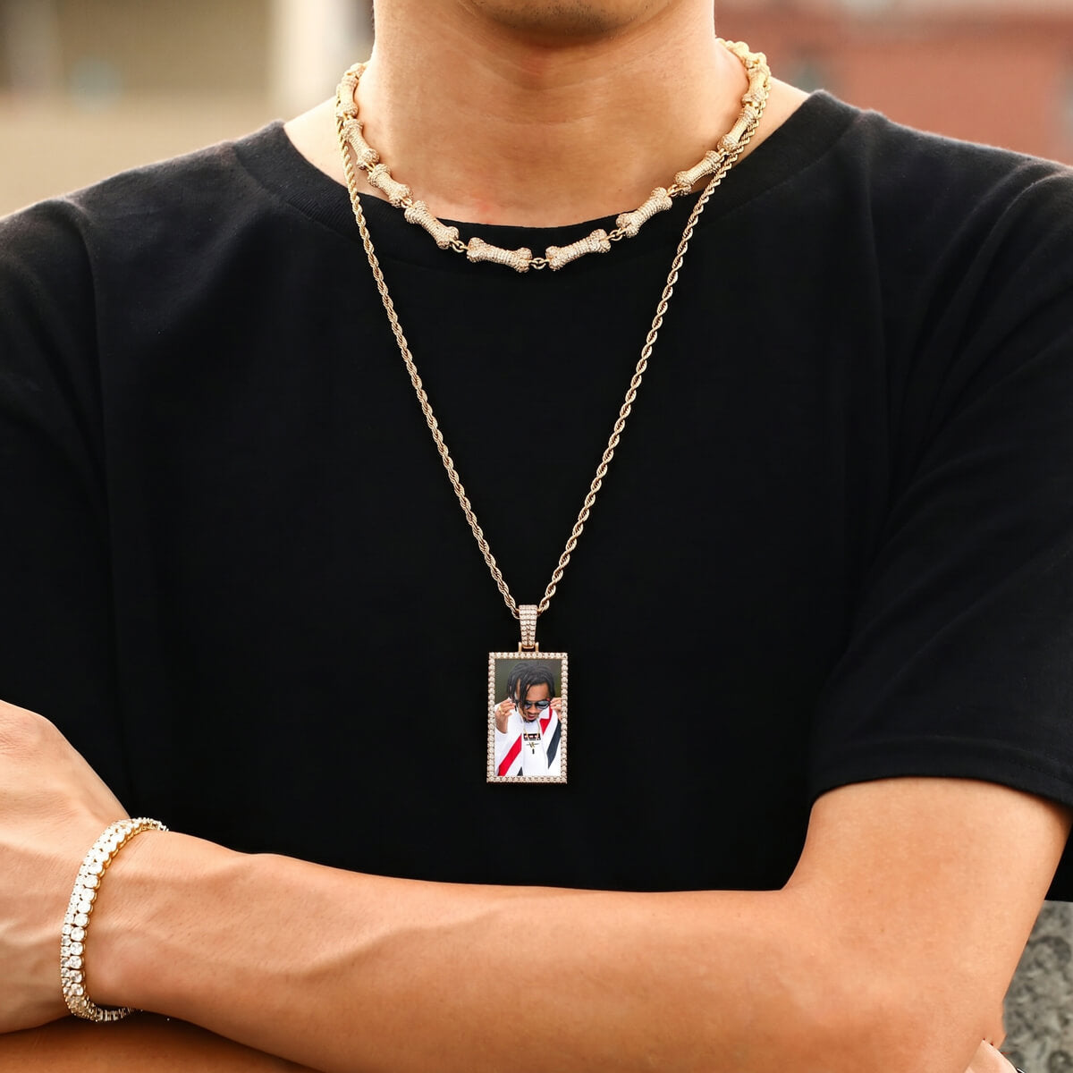 Person wearing a black shirt with a gold chain necklace featuring a pendant with a photo on it. picture necklace for men